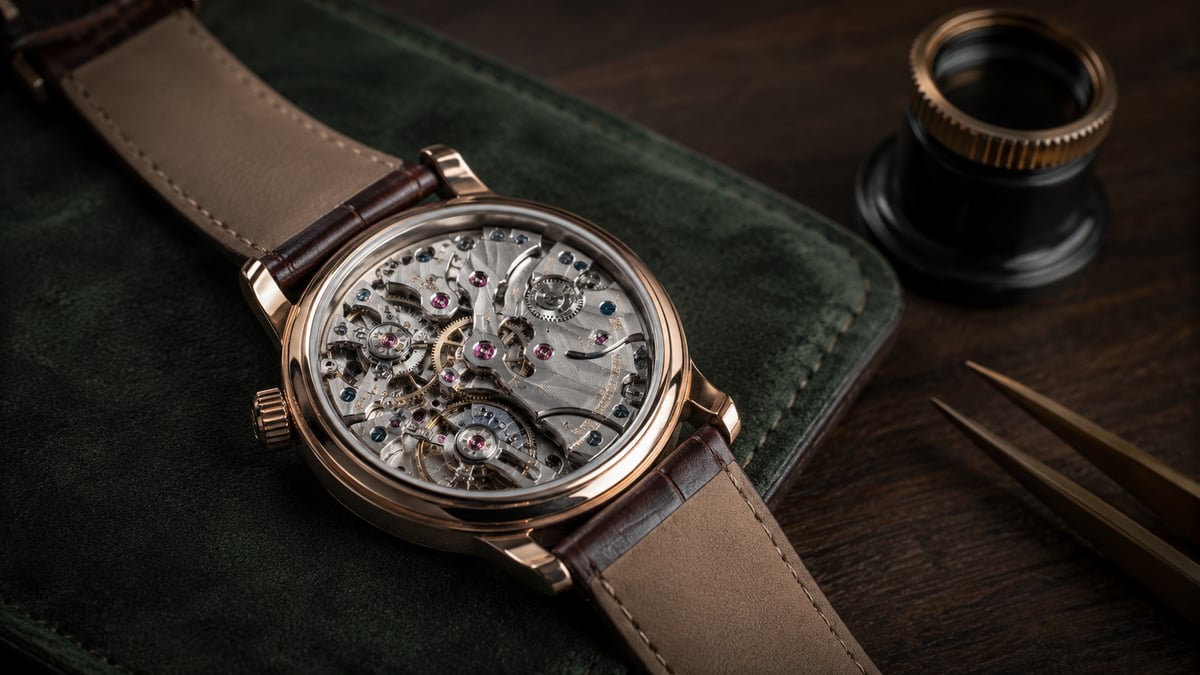 Open-back luxury wristwatch with visible mechanical movement, jeweler's loupe, and watchmaking tools on a dark wooden surface, illustrating watch authentication inspection